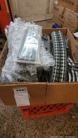 Box with assorted straight and curved model train track sections, some packed in blister packaging and others loose, all sitting inside a cardboard box.