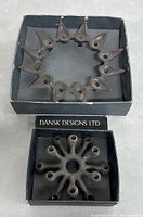 Two cast iron candle holders in original boxes on grey background. Larger starburst and smaller spider style.