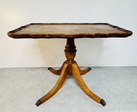 Front view of antique wooden tilt top table with scalloped edges and brass lion paw feet on casters.