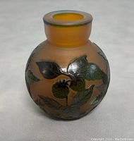 Front view of the round cameo art glass vase showing greenish leaves and berries on a frosted amber background with a narrow neck and rounded body.