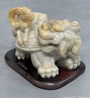 Front angle view of the Shoushan stone lion with a ram on its back, showing detailed carving and wooden base.