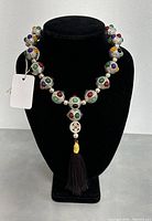 Full front view of the white copper beaded rosary displayed on black stand showing beads with multicolored stones and attached tassel.