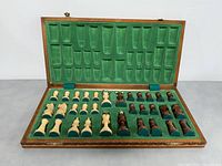 Hand-carved wooden chess pieces stored in a green felt-lined wooden case, showing both light and dark pieces arranged in rows.