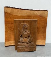 Wooden ascetic Buddha carving displayed in front of live edge cheese board showing details of carving and background wood board.