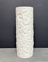 Front view of white matte porcelain vase showing fossil ammonite raised designs.