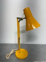 Yellow adjustable desk lamp shown from side with lamp off. Visible metal springs on arm.