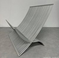 Side angled view of the silver metal folding magazine rack showing its curved vertical slats and folding design.