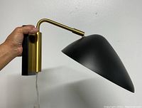 Side view of the wall lamp held to show dimensions and curved arm ending in a pointed black shade.