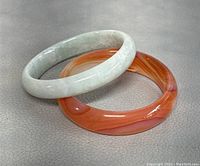 Photo shows green jade bangle and orange glass bangle side by side on gray background.