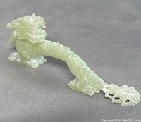 Clear view of the full length of the carved dragon figurine on a gray textured surface, showing the detailed scales and body shape.