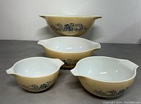 Set of four Pyrex nesting mixing bowls in Homestead Cinderella pattern, beige exterior with blue floral pattern and white interior, stacked with the largest bowl on top.