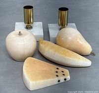 Pair of stone decorative fruit items and two stone candle holders on a grey surface