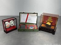 Photo showing the full lot with the calligraphy set opened, the two hand-painted eggs in glass display case, and the yellow floral carving in its glass case with red background