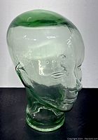 Side view of translucent green glass mannequin head with detailed facial features and minor wear visible, showing overall shape and color.