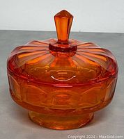 Vintage Viking Amberina orange glass candy dish with diamond point pattern and lid with faceted knob handle, shown on gray surface.