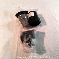 Two black reusable Keurig coffee filter cups shown on white background, one still wrapped in clear plastic.