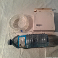 Top-down view of the tape roll partially wrapped in plastic beside its open white box, with a water bottle for scale.