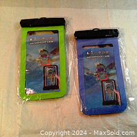Two waterproof phone cases in packaging; one green-bordered, one blue-bordered, both include lanyards and clear fronts.