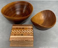 Photo showing the two wooden bowls and the small Native New Zealand wooden box together on a grey surface. Highlights wood grain and finished surfaces, and box inlay.