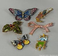 Overview of all six brooches laid out on grey surface, showing designs and colors