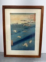Full view of the framed woodblock print titled "White Heron" depicting white herons flying over a blue riverland landscape with houses, trees, and mountains in the background.