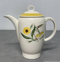 Front view of the white porcelain teapot showing the marigold flower design and yellow trimmed lid.