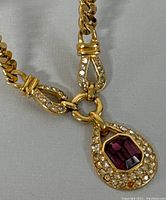 Close-up of pendant showing gold-tone metal, clear rhinestones, and central purple gem.