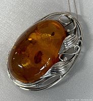 Close-up showing the amber stone and 925 silver detailed setting of the pendant with leaf design.