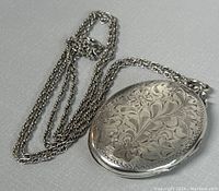 Front view of oval locket showing floral engraving and attached chain