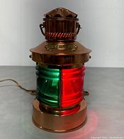 Front view of the copper and brass maritime ship lamp with visible green and red lenses lit up on a grey surface.