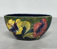 Front view of vintage Moorcroft ceramic bowl showing detailed colorful hand-painted flowers with yellow and red hues on green background.