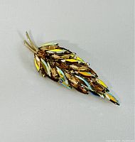 Front angle view of a leaf-shaped brooch with amber and aurora borealis marquise rhinestones on gold-tone metal.