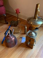 All seven brass and copper items arranged on the floor showing teapot, candleholder, trivet, grinders, and fondue pot.