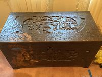 Full view of the carved wood chest showing top and front with carvings and brass hardware.