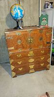 Front view of medium brown wood chest with brass hardware. Two top doors and four drawers below. Globe and other objects on top not included.