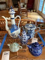 Overall view of five Asian teapots on glass surface, showing variety of shapes and blue and white glaze.