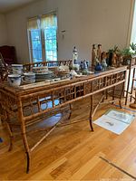 Angle view of the bamboo side table with various blue and white ceramics and small wooden figurines displayed on top. Hardwood floor and window in background.