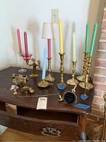 Overview of brass and glass candlestick holders with assorted colored candles and two brass snuffers on wooden table.