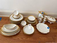 Full overview of the entire set including plates stacked, cups, gravy boat, and covered dish showing lot contents and gold rim detail