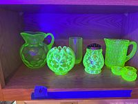 Seven pieces of uranium glass on shelf under UV light revealing bright green fluorescence