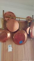 Five copper pans and two lids hanging on brass rack against wall