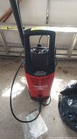 Front view of the Husky power washer showing handle, front vents, power cord and some hose.