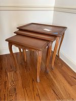 Three wooden nesting tables stacked, showing size differences and carved details on legs and edges.
