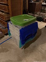 Seven clear plastic storage containers stacked in basement with green, blue, and turquoise lids visible