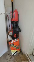Homelite pole saw and Black & Decker Leaf Hog blower vac boxed and leaning in corner