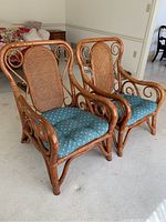 Two rattan chairs with curved armrests, cane backrests, and blue removable cushions placed side by side in carpeted room.