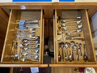 Wooden drawers filled with various silverplate flatware pieces arranged by type including knives, forks and spoons.