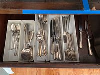 Five plastic storage trays in drawer holding assorted forks, spoons, knives, carving set