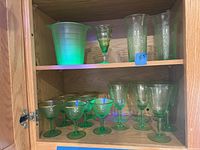 Overall view of glassware set including ice bucket on upper shelf and assortment of green stemware glasses below.