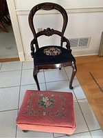 Full view of vintage carved wood chair with black needlepoint floral seat and matching coral pink needlepoint foot stool with floral embroidery.